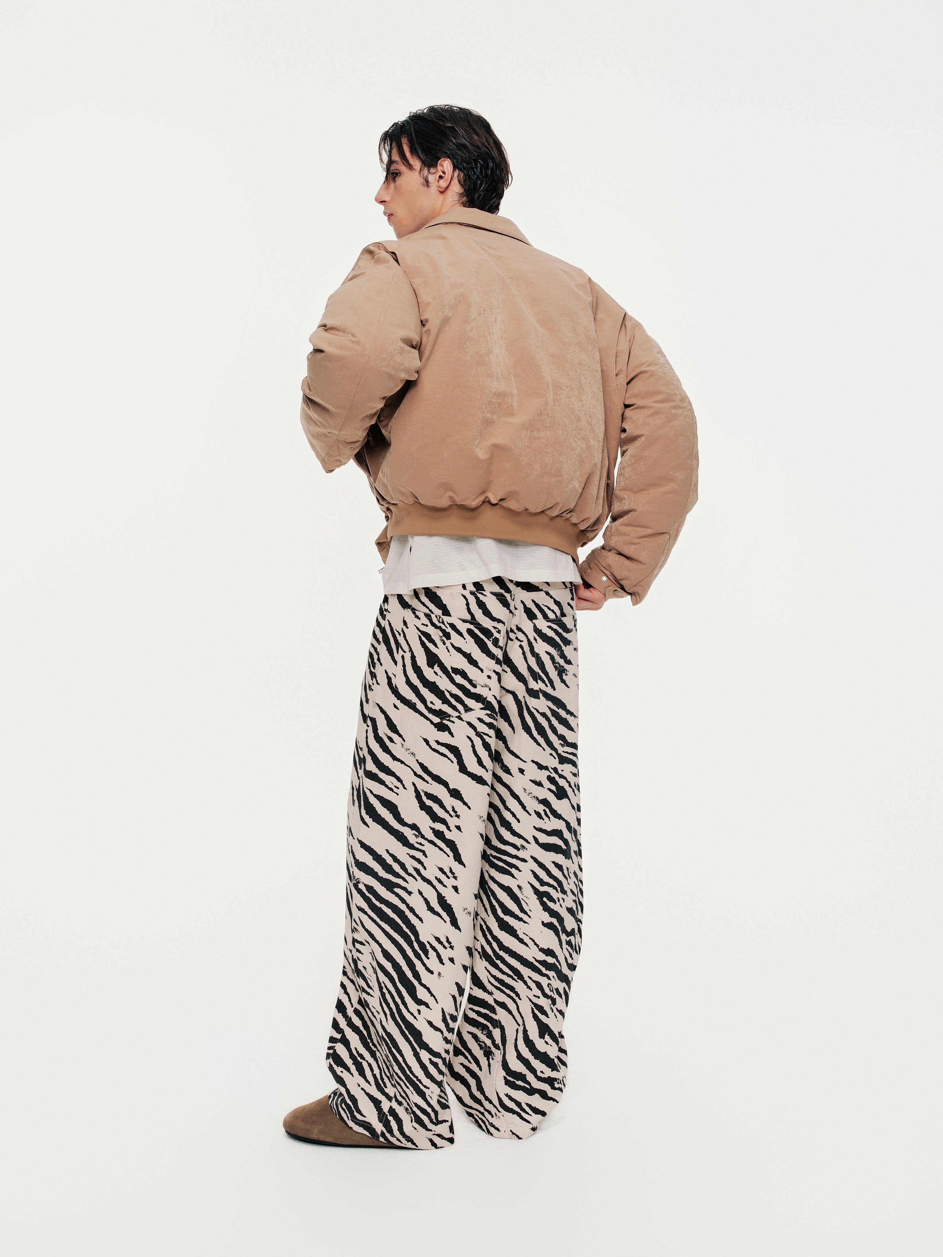 Person wearing a beige jacket and zebra print pants on a white background