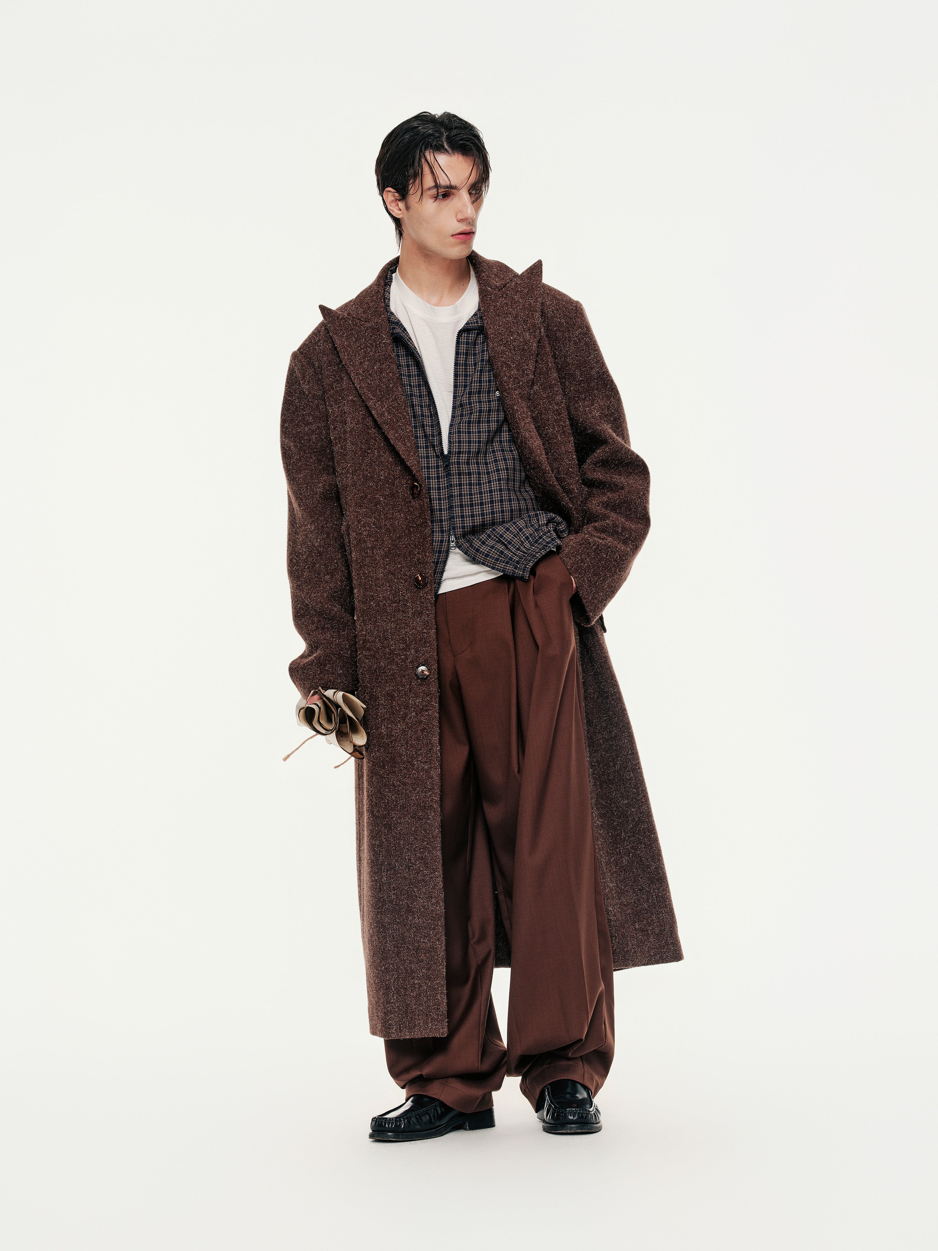 Person wearing a long brown coat and pants on a white background