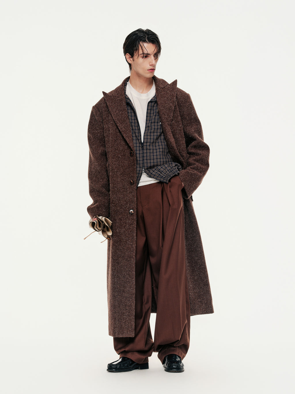 Person wearing a long brown coat and brown pants on a white background