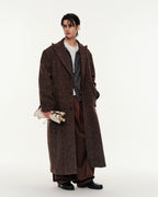 Man wearing a long brown coat holding a patterned bag on a white background
