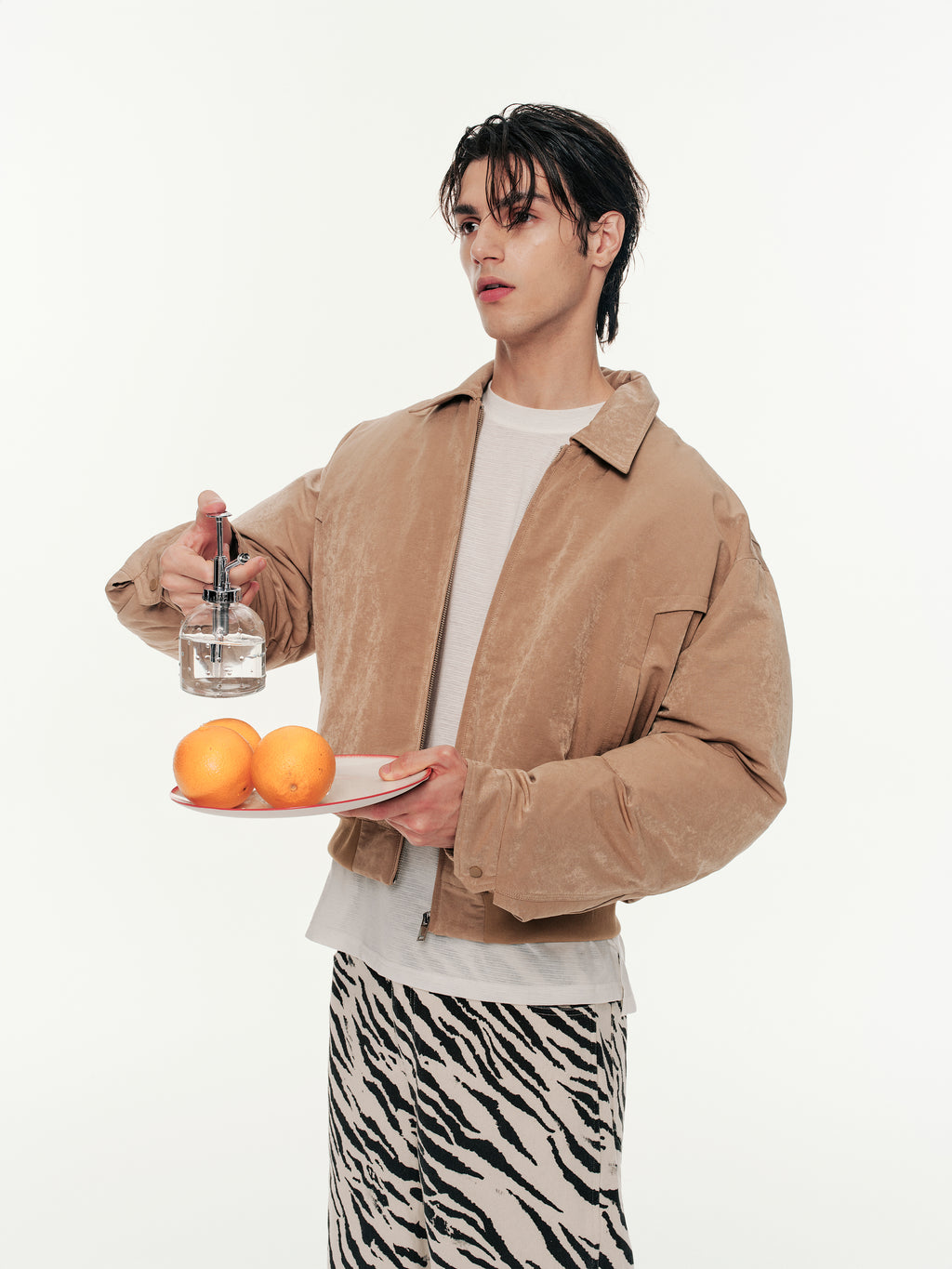 Person holding a plate with oranges and a bottle on a white background