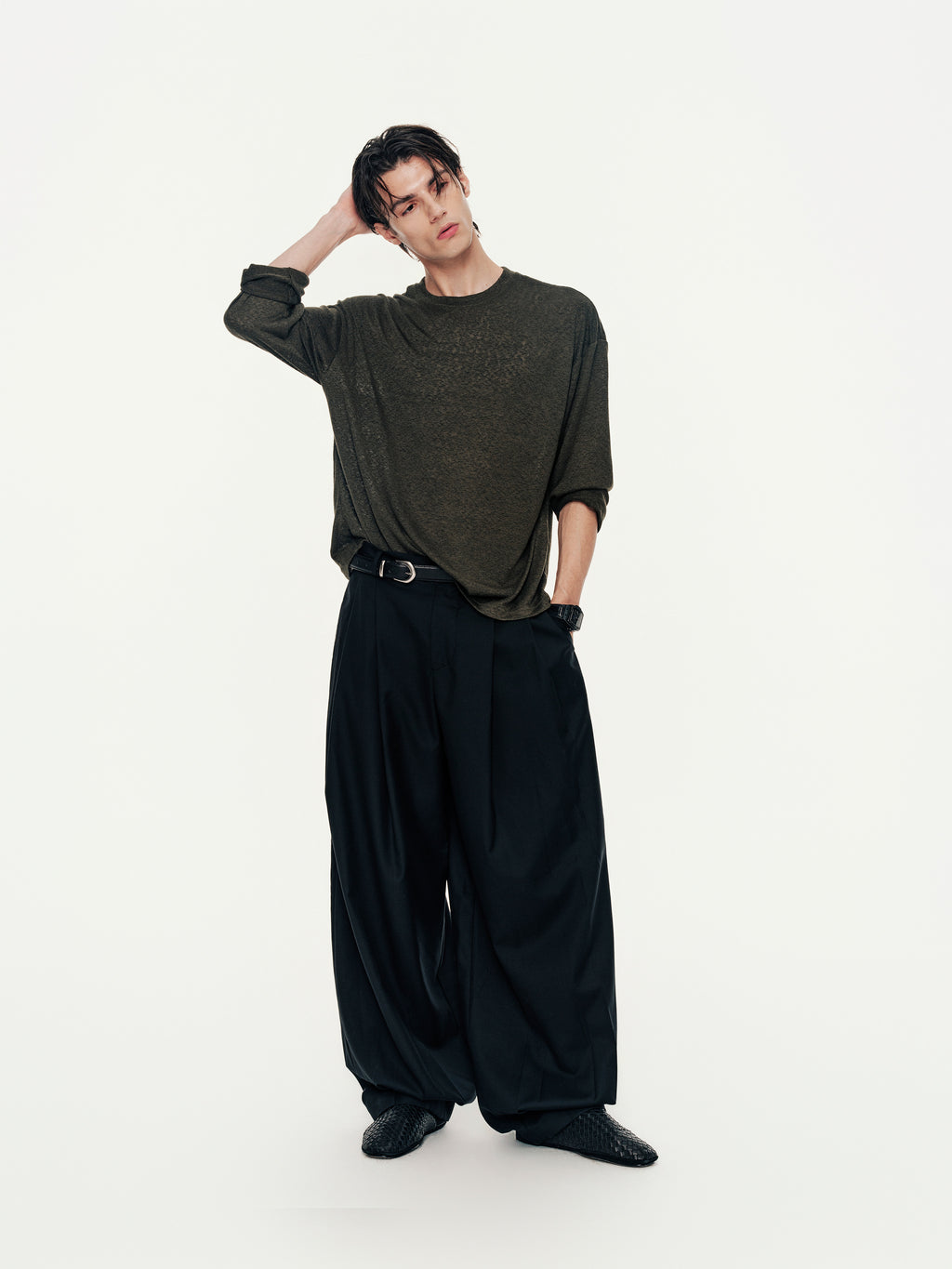 Person wearing a dark green sweater and black wide-leg pants on a white background