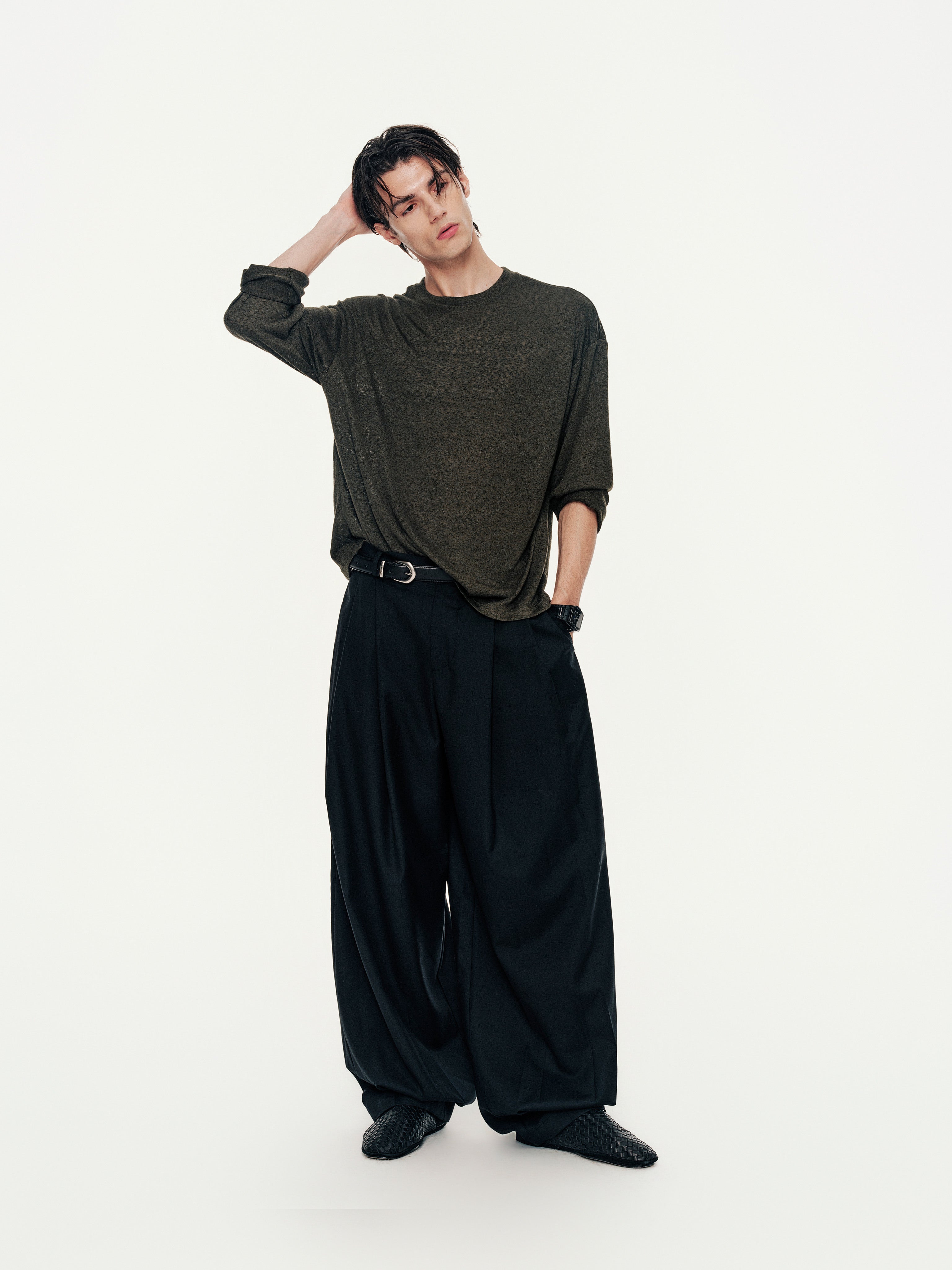 Person wearing a dark green sweater and black wide-leg pants on a white background